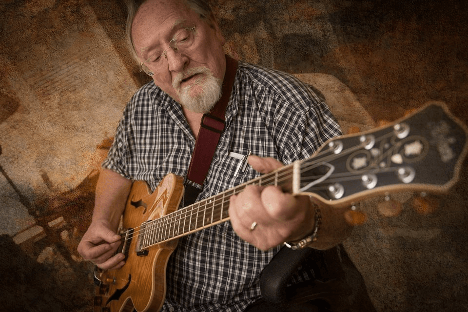 Paul Jones Sr. seated and playing his guitar.